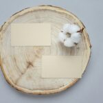 Top view of two blank business cards on a round wooden coaster with cotton, perfect for design mockups and presentations.